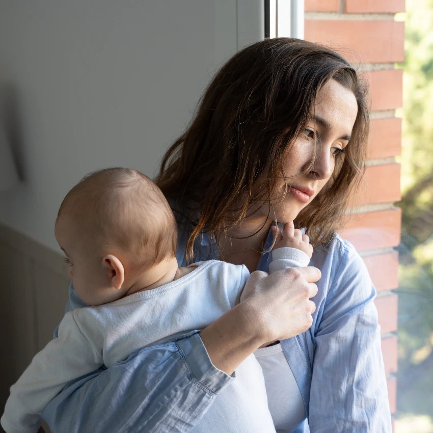 serious mom holding baby looking out window