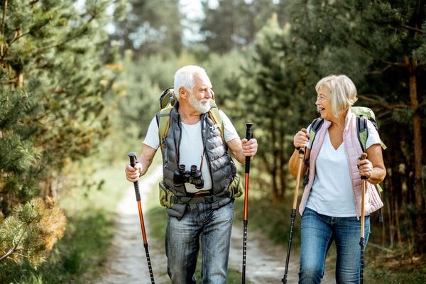This may contain: an older couple walking down a path in the woods with backpacks and hiking poles
