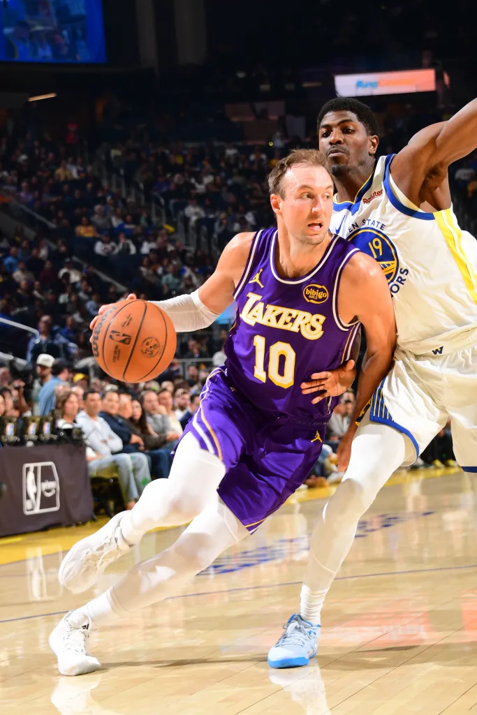 A Lakers player dribbles past a Warriors player.