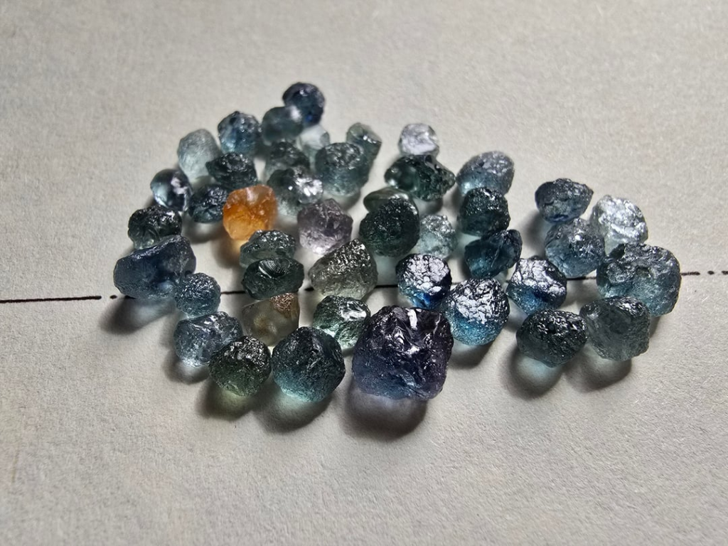 Pile of raw, uncut sapphires in various shades of blue, green, purple, and orange.