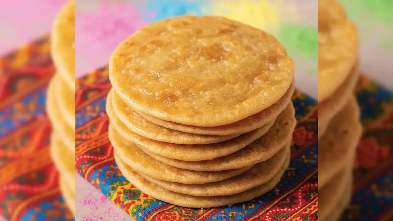 Stack of golden, crispy puris placed on a colorful traditional cloth.