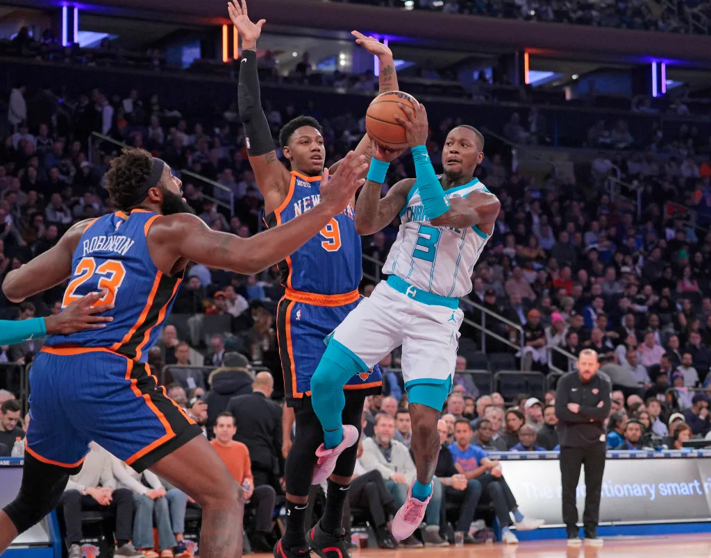 Charlotte Hornets guard Terry Rozier jumping to make a pass in front of two New York Knicks players.