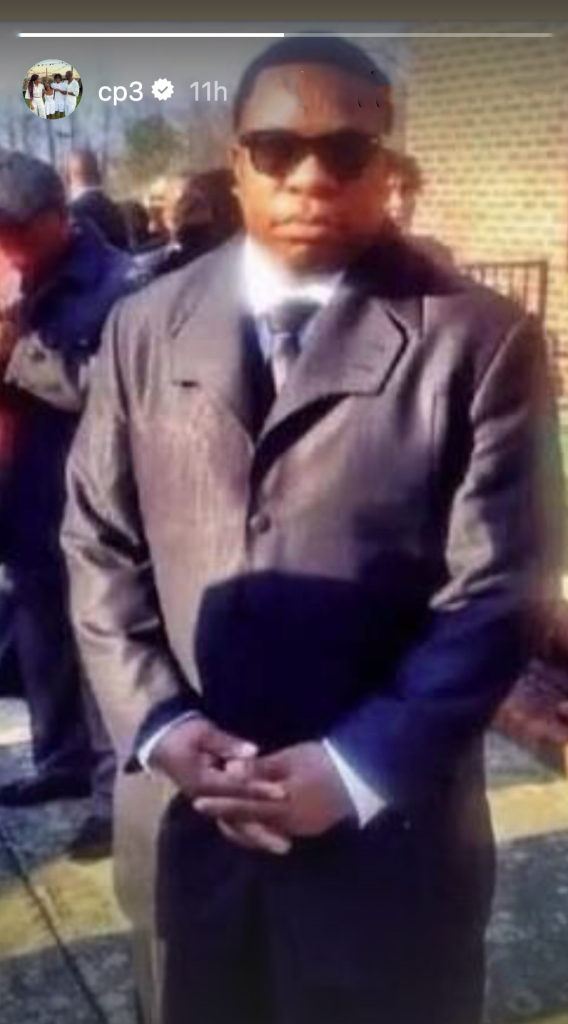 Man in a suit and sunglasses, with hands clasped in front of him.