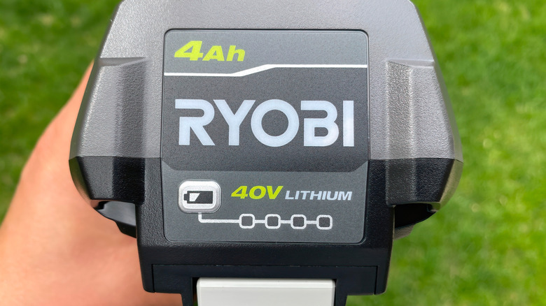 A hand holding a 40V Ryobi power tool battery