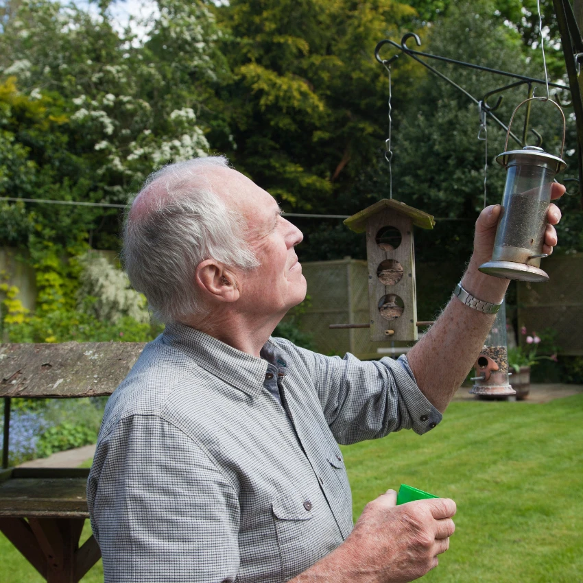 man refilling birdfeeders as part of his longevity fitness routine for his brain