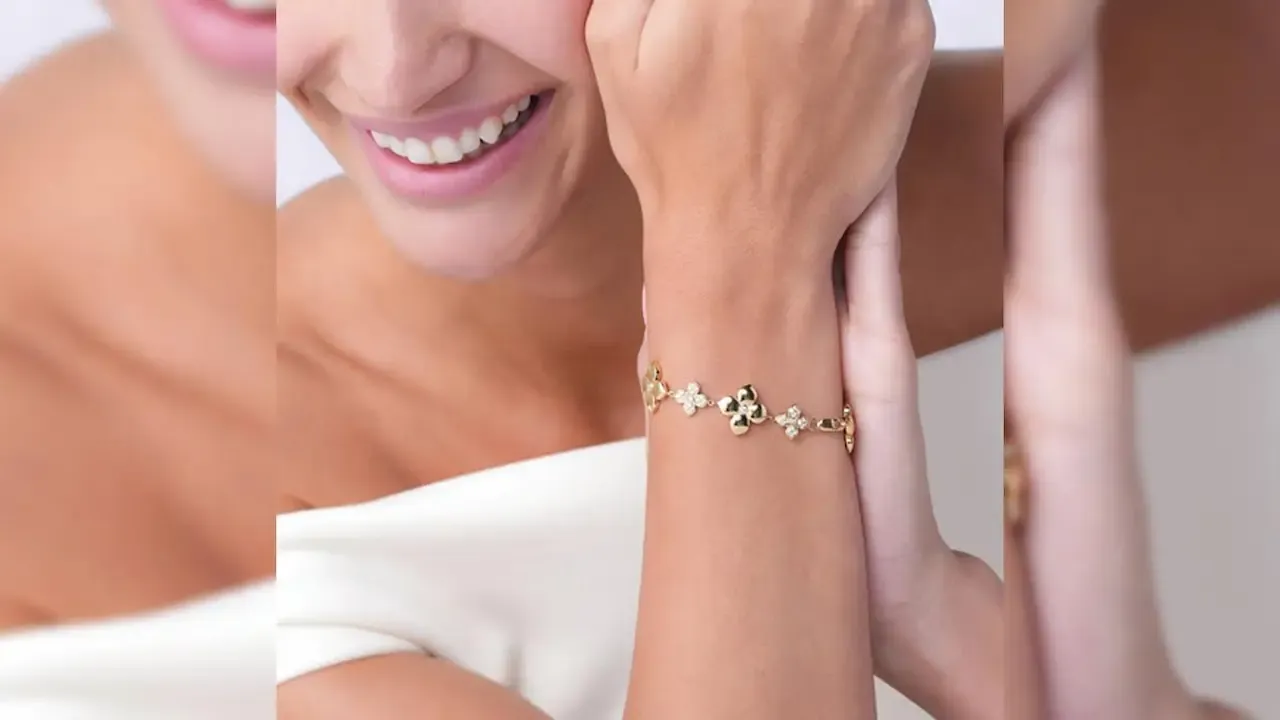 Close-up of a smiling woman wearing a delicate gold bracelet with small floral-shaped charms on her wrist, her hand gently resting near her face.