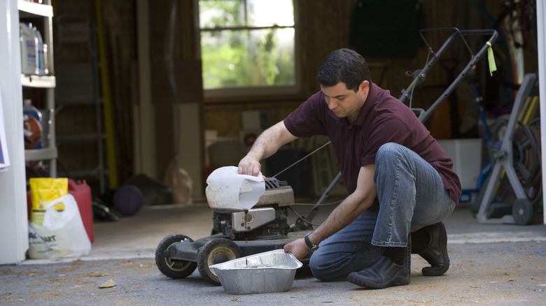 Man in the process of changing his lawnmower's oil outside a garage