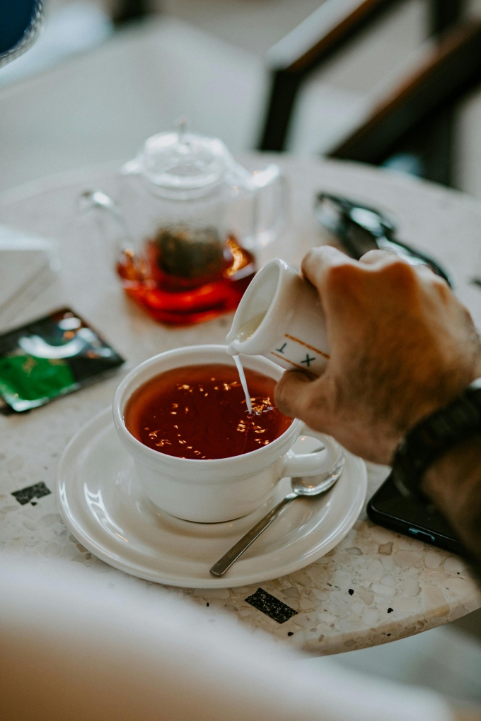 A hand pouring milk into tea. Photo by Pexels
