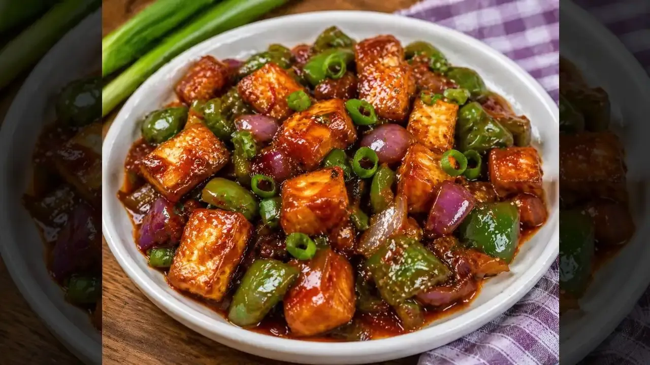 Spicy chili paneer with bell peppers and onions in a glossy sauce, garnished with spring onions.