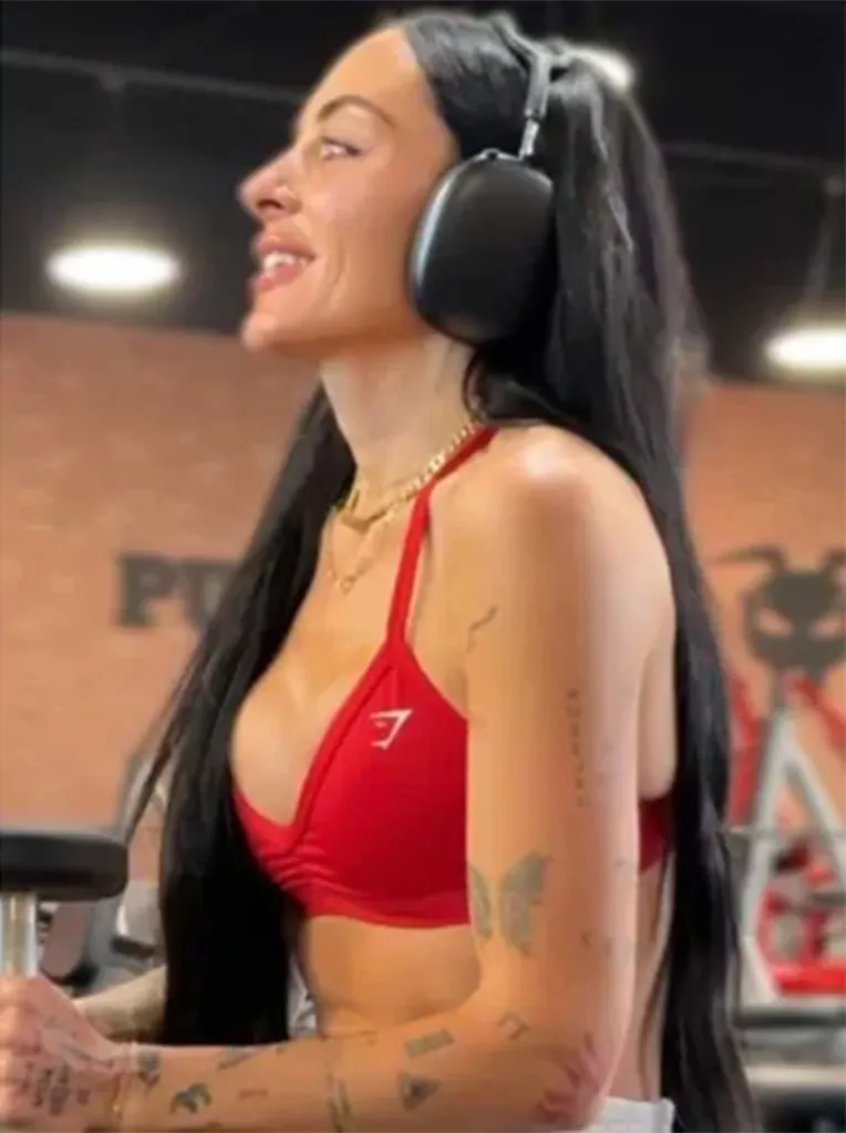 A woman in a red sports bra and large headphones, looking to the side with her hair falling over her shoulders.
