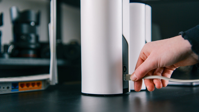 A person's hand inserts an ethernet cable into a sleek, white mesh Wi-Fi node