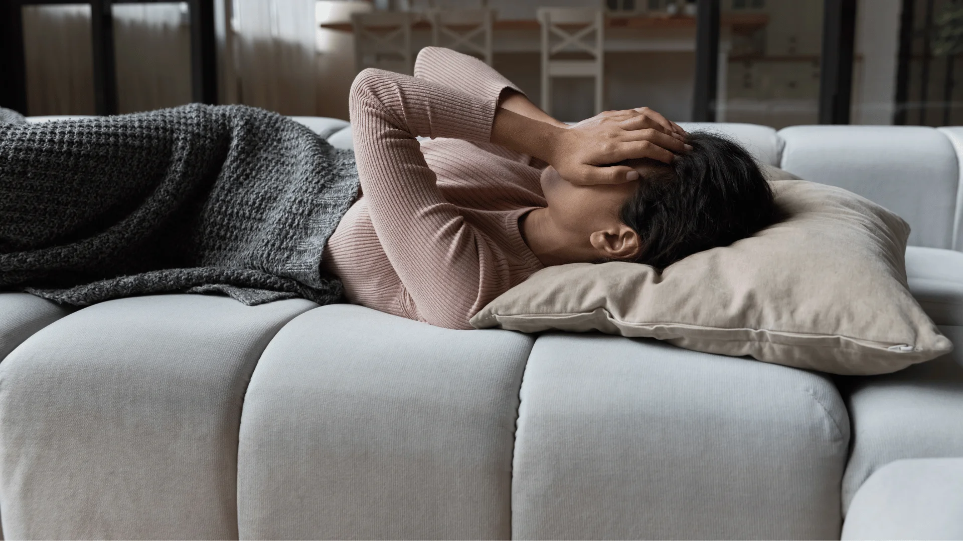 Woman who needs a break looks exhausted on a couch with hands over her eyes