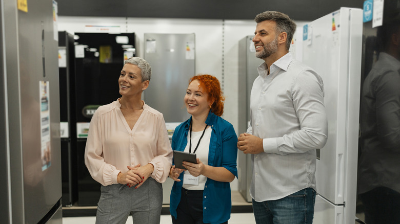 A smiling couple looking at a refrigerator with a smiling saleswoman