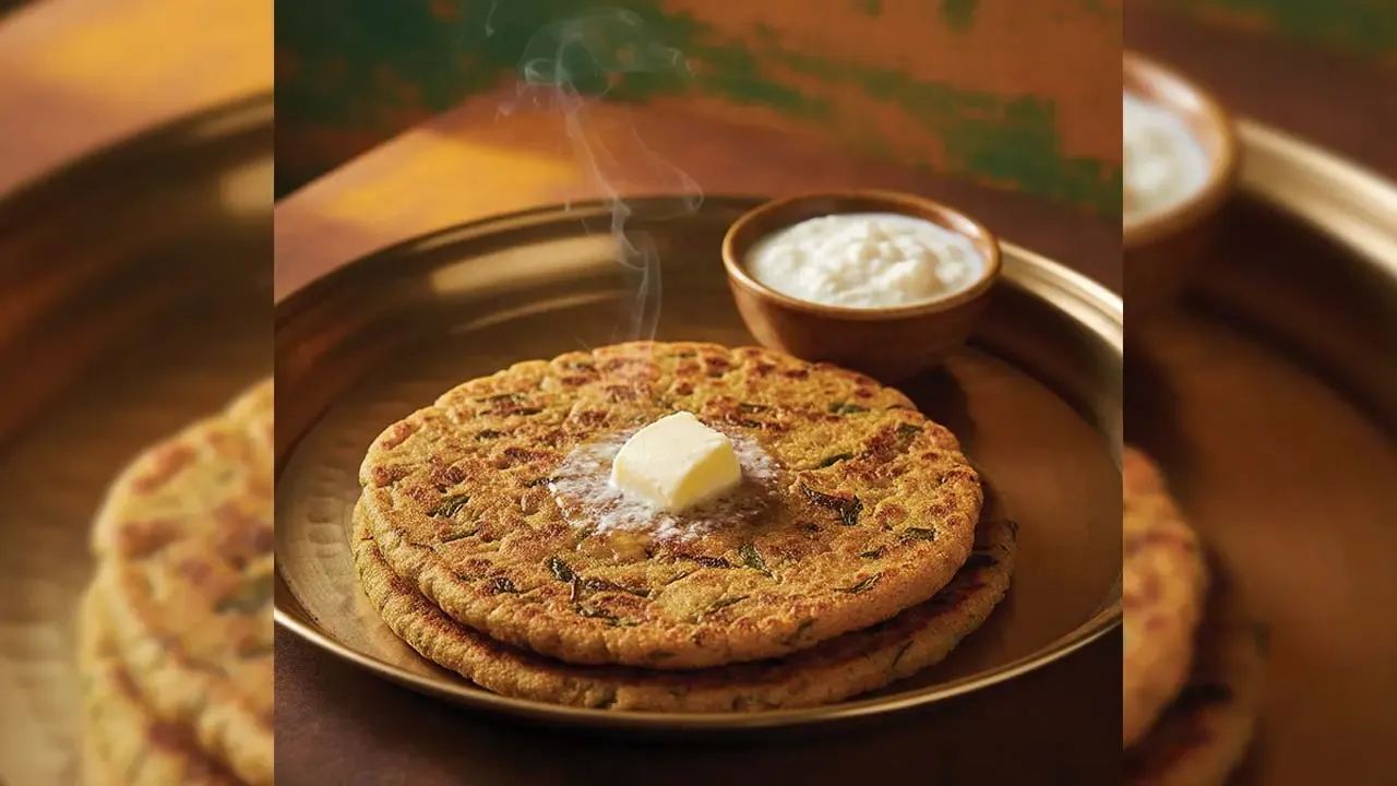 Two steaming hot, golden-brown flatbreads or parathas topped with a melting cube of butter, served in a traditional brass plate next to a small wooden bowl of fresh curd or yogurt
