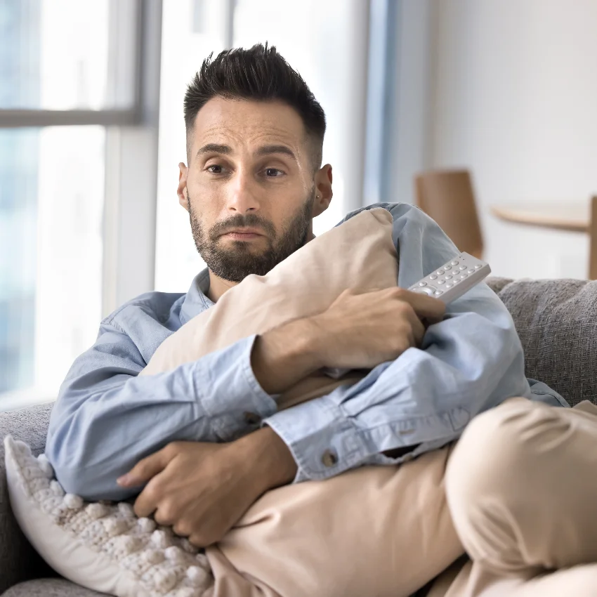 man hugging pillow watching horror movie