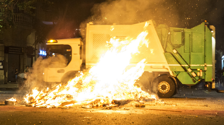 A large fire in front of a parked garbage truck