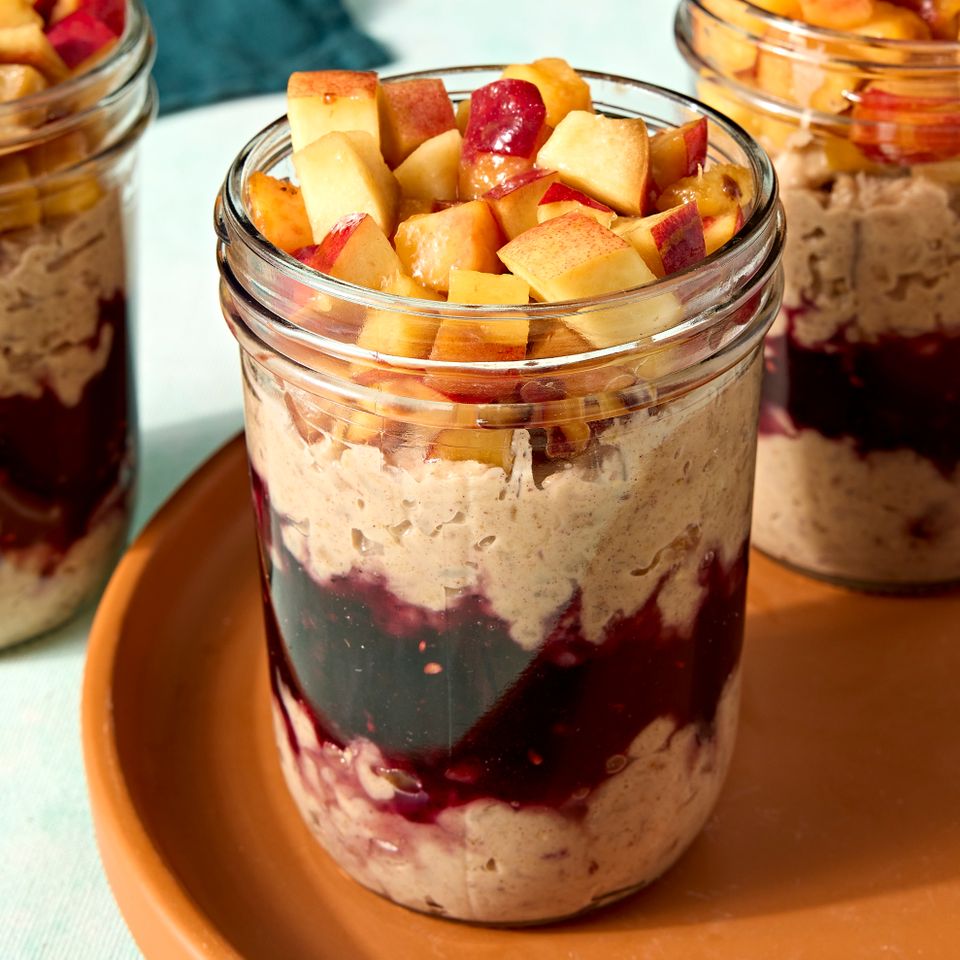 A jar of overnight farro with layers of fruit and grains topped with chopped fruit on a tray next to other similar jars Credit: Photographer: Jen Causey.