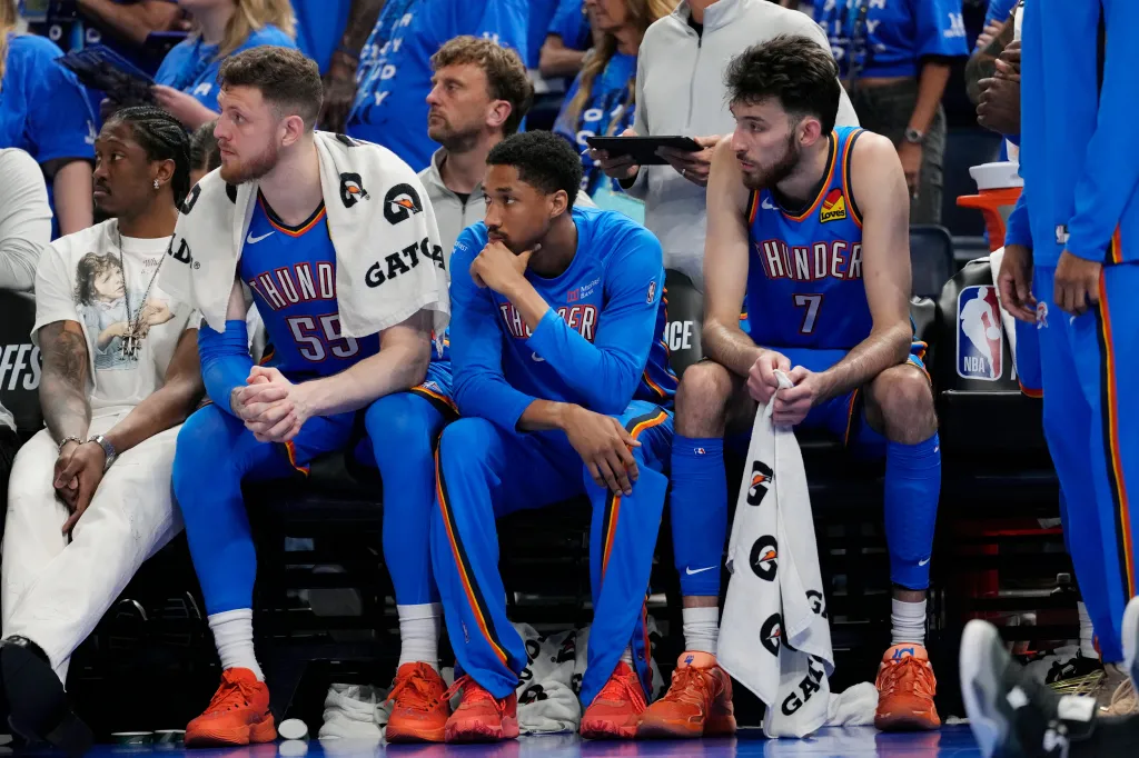 Oklahoma City Thunder players Isaiah Hartenstein, Aaron Wiggins, and Chet Holmgren watch from the bench during a game.