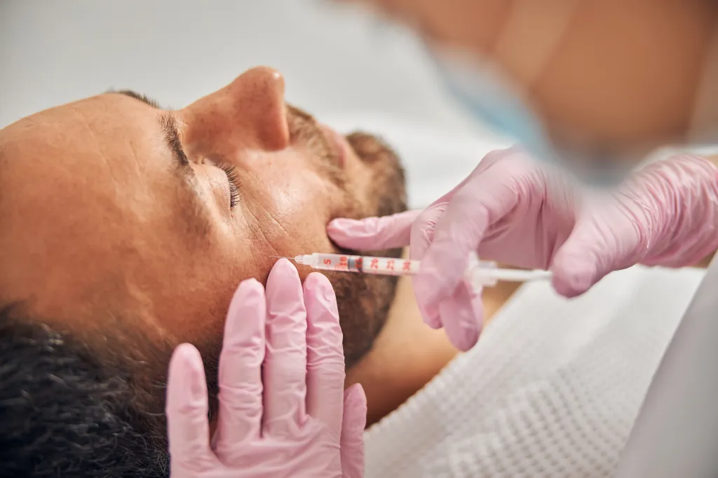 A man receiving an injectable skincare treatment from a cosmetologist.