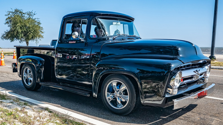 A black 1956 Ford F100 parked on the side of a road