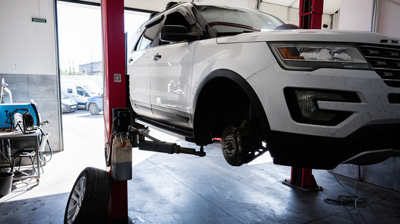 White Ford Explorer being repaired in a shop with the front wheel removed