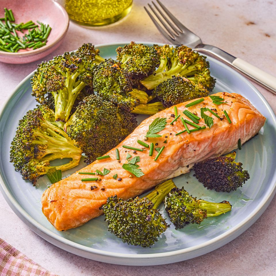 A plate of baked salmon topped with herbs served alongside roasted broccoli Credit: Ali Redmond