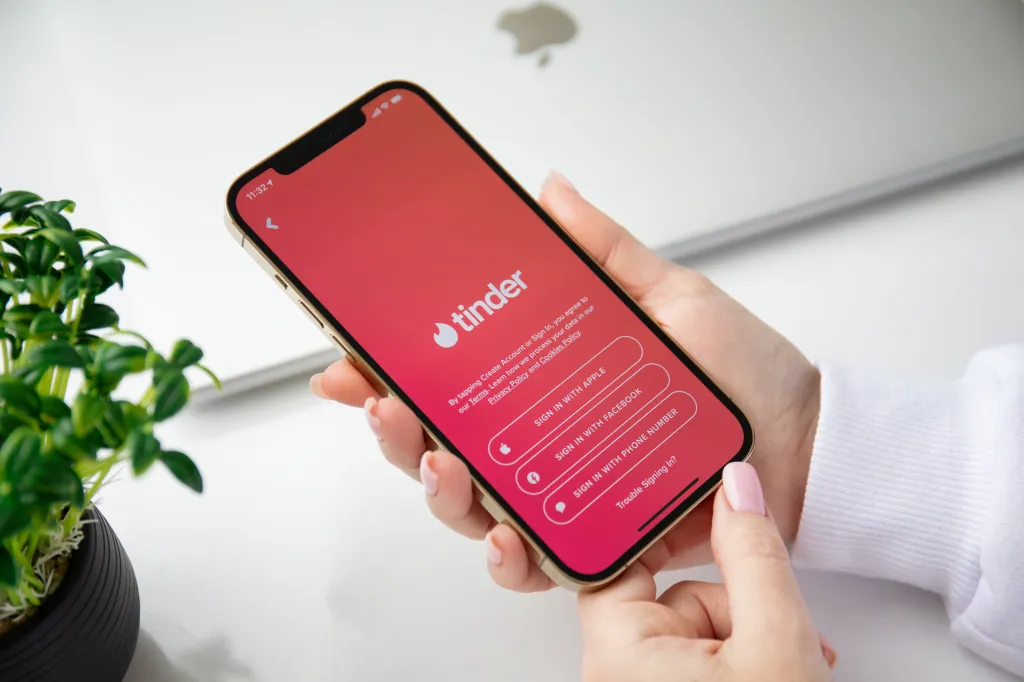 Woman holding a gold iPhone 12 Pro Max displaying the Tinder app sign-in screen.