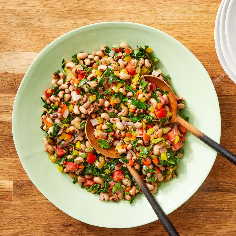 Spicy black-eyed pea & collard green salad in a light green bowl with two wooden servings spoons Credit: Photographer: Rachel Marek, Food Stylist: Holly Dreesman