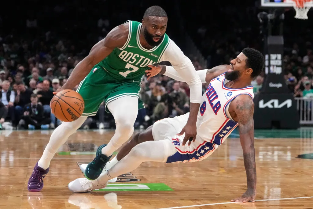 Jaylen Brown dribbling past Paul George who is on the ground.