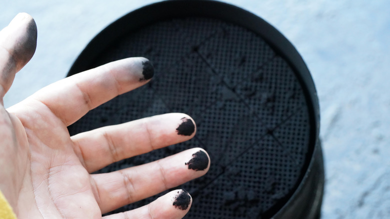 Hand stained with soot with dirty DPF in background