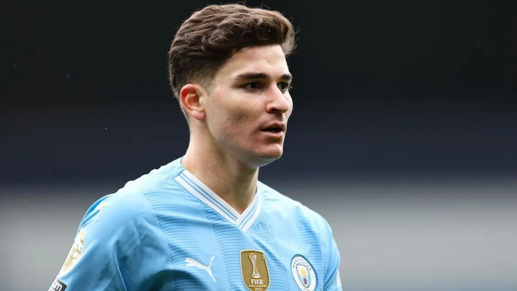 Julian Alvarez in a blue Manchester City kit, looking thoughtfully during a match.