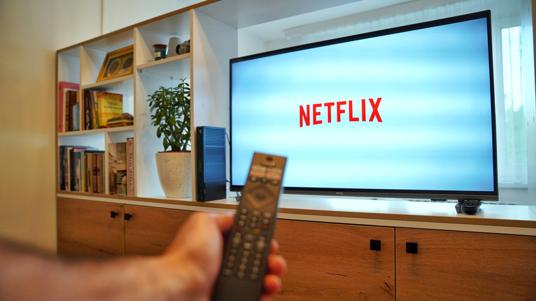 A person holding a remote in front of a smart TV opening the Netflix app