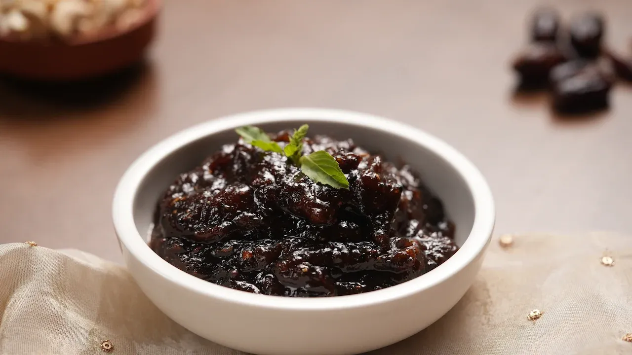 Traditional Khajur Khatta, a sweet and tangy Odia date chutney prepared with dates, jaggery and spices, garnished with fresh holy basil for Jagannath Rath Yatra.