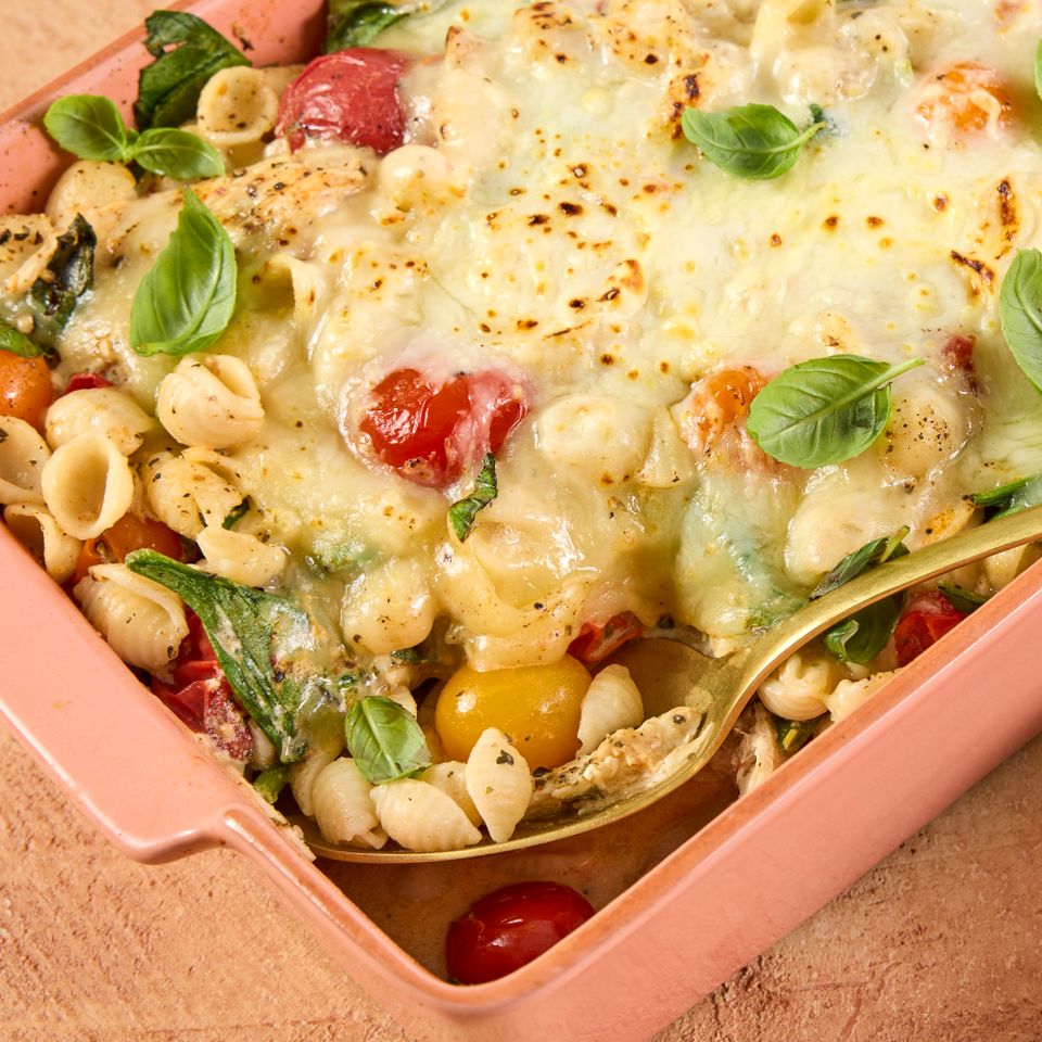 A baked pasta dish with cheese cherry tomatoes basil and a golden spoon in a pink baking dish Credit: Photographer: Jen Causey, Food Stylist: Margaret Monroe Dickey, Prop Stylist:Hannah Greenwood