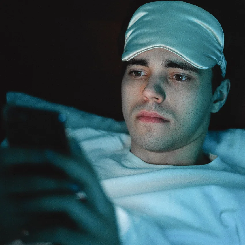 Man lying awake in bed at night while scrolling through his smartphone before going to sleep