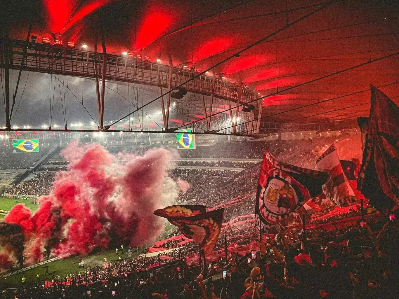 Flamengo fans with red flares and flags filling the Maracana stadium under a red illuminated roof