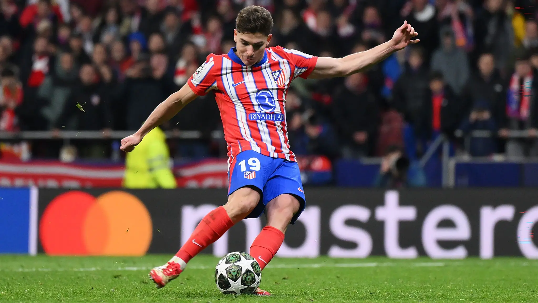 Julian Alvarez in an Atletico Madrid kit kicking a soccer ball during a match