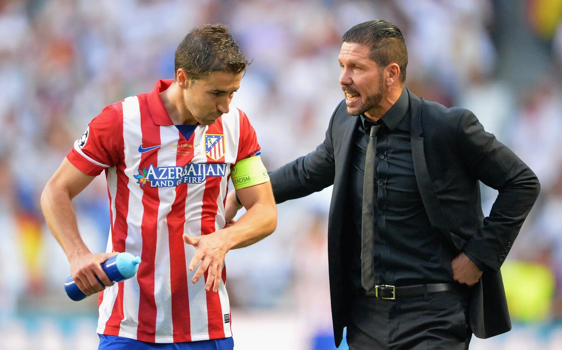 Diego Simeone in a black suit speaking to an Atletico Madrid player in a red and white striped jersey