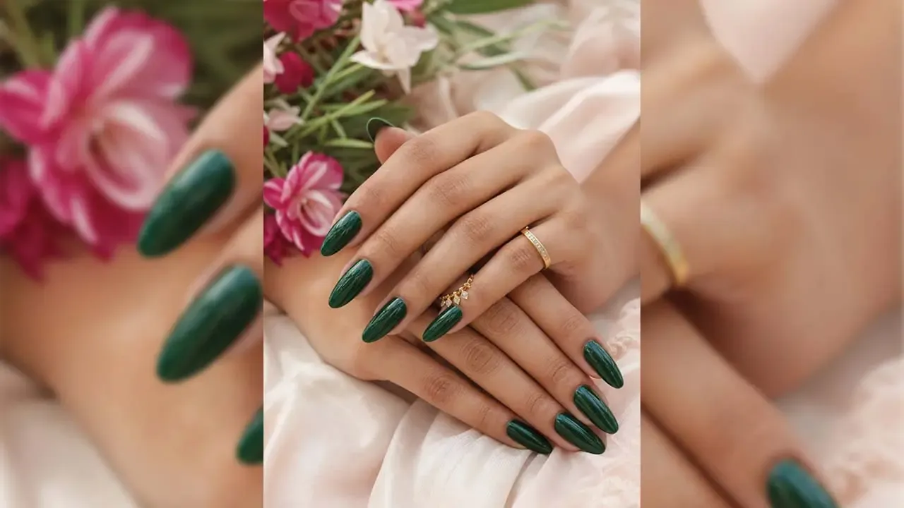 Woman displaying long glossy dark green manicured nails with gold ring accents placed against a soft floral background.