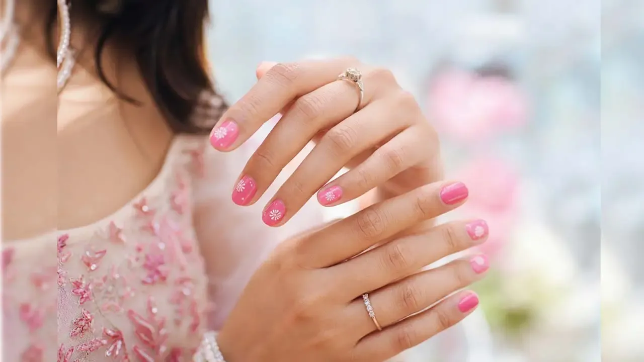 Woman displaying elegant bright pink manicured nails decorated with delicate white floral art and subtle rings setup.