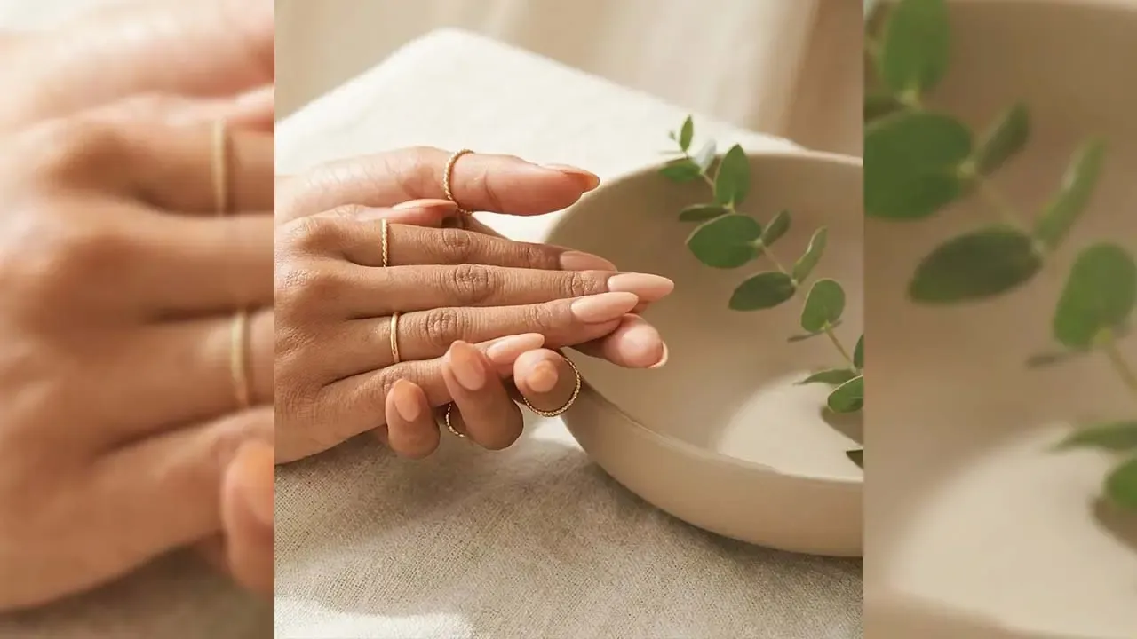 Woman showcasing minimal peach nude manicured nails adorned with thin gold rings beside a ceramic bowl setup.