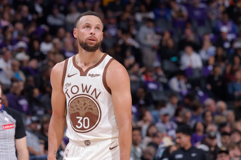 Stephen Curry looking up while wearing a white and brown basketball jersey with "The Town" written on it.