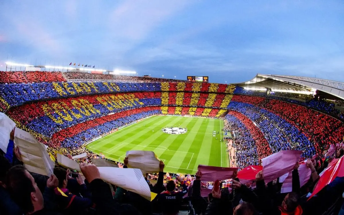 Wide view of Camp Nou stadium with fans creating a blue, red, and yellow mosaic in the stands