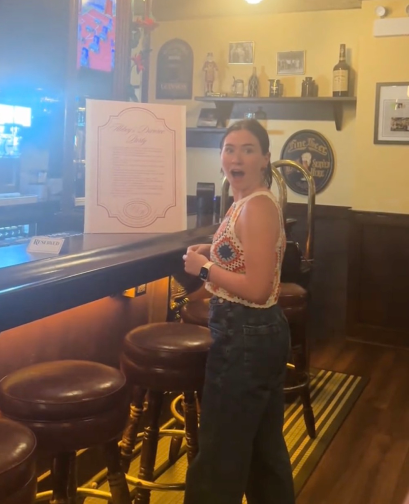 Woman looking surprised at a sign for her divorce party at a bar.