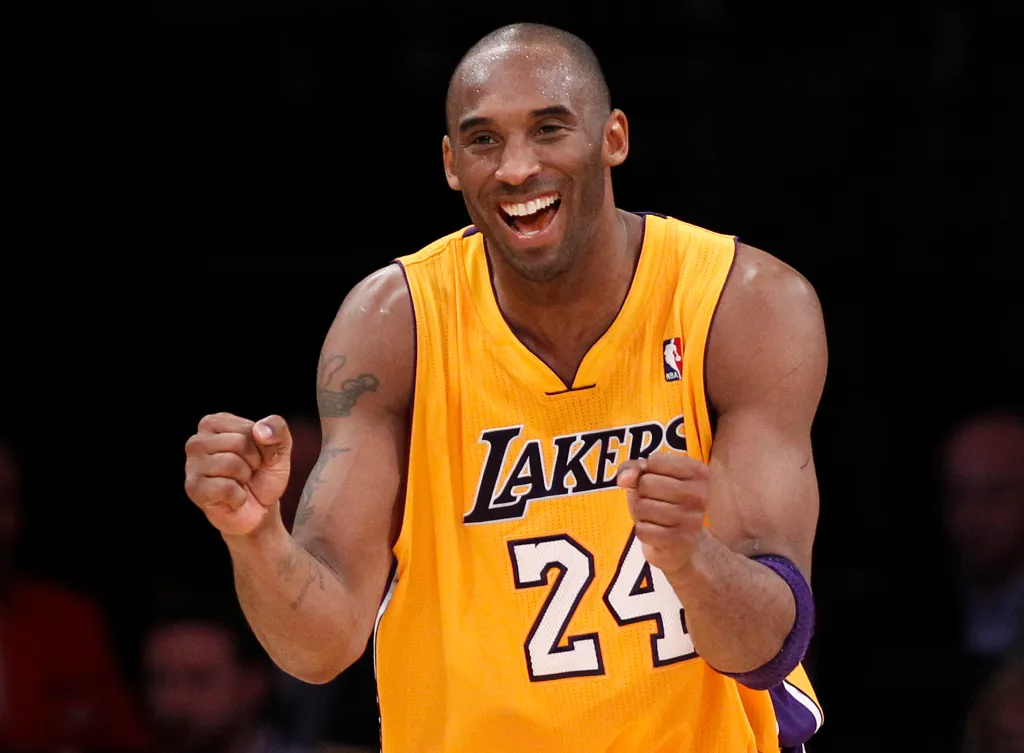 Kobe Bryant smiling and flexing both arms in his Lakers jersey.
