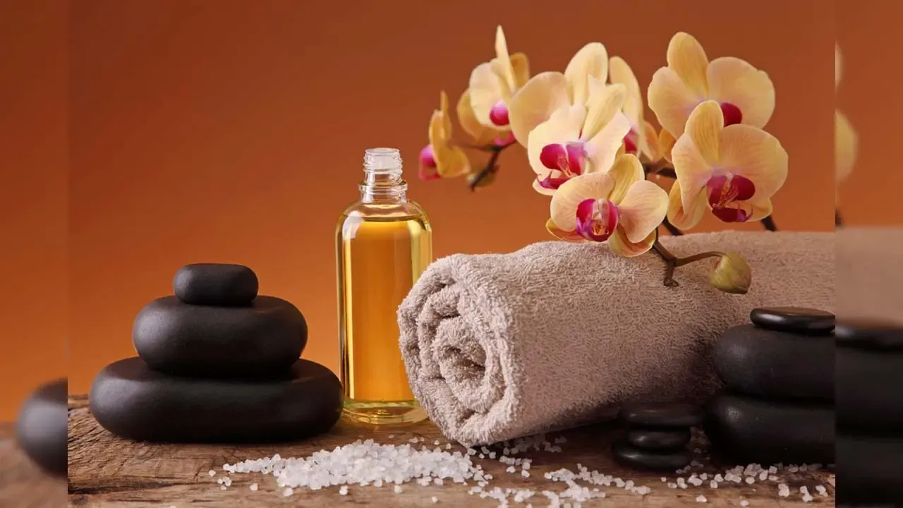 Essential oil bottle rolled towel black hot stones yellow orchid flowers and sea salt on wooden table setup.