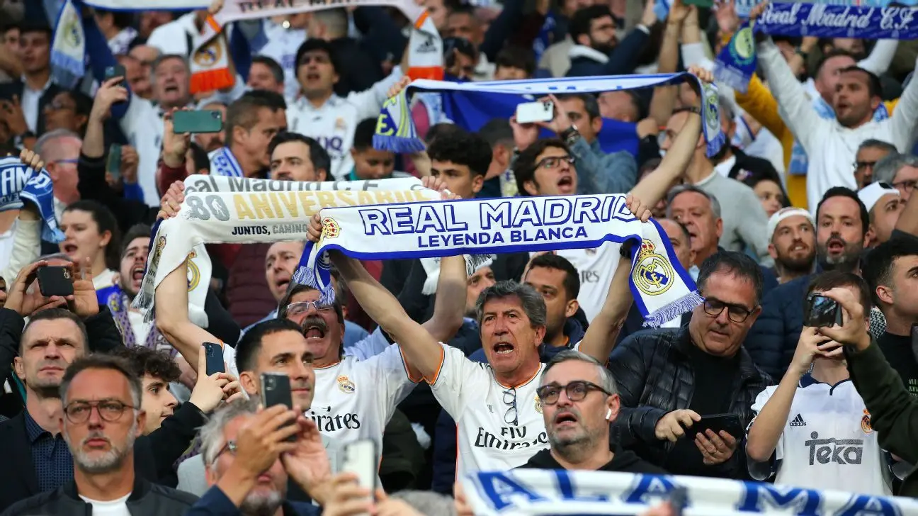 Real Madrid fans cheering and holding white and blue scarves in the stands of the Santiago Bernabeu stadium