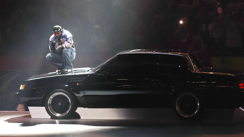Side view of Kendrick Lamar crouching on a Buick Grand National on stage