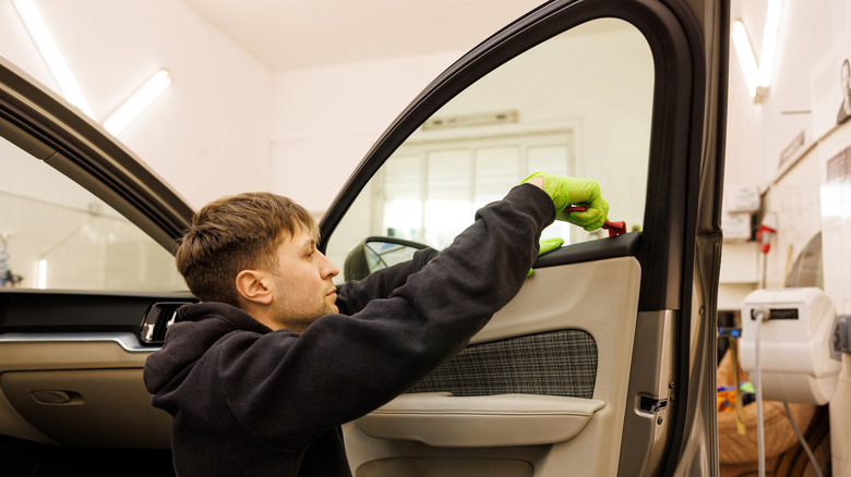 Technician servicing right-side front car door, pictured with special removal tools for window trim pieces