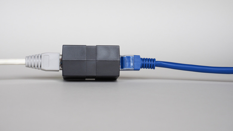 black RJ45 ethernet coupler being used to connect two white and blue LAN cables
